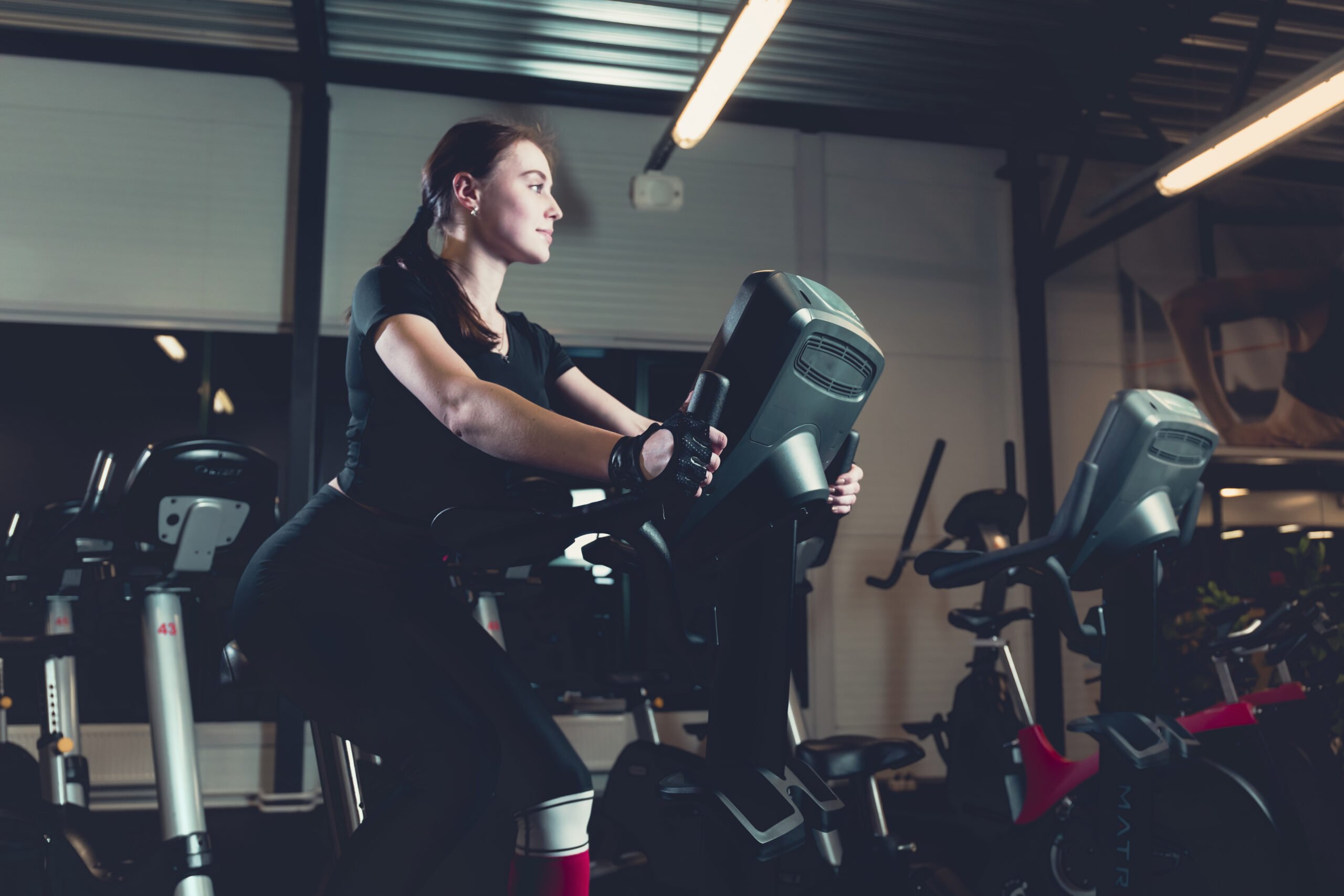 side-view-young-woman-riding-exercise-bike-gym-scaled.jpg